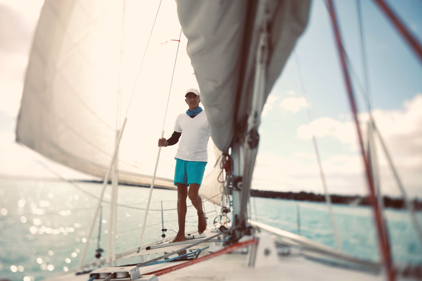 Sailor standing on the bow of a sailboat, between the sails